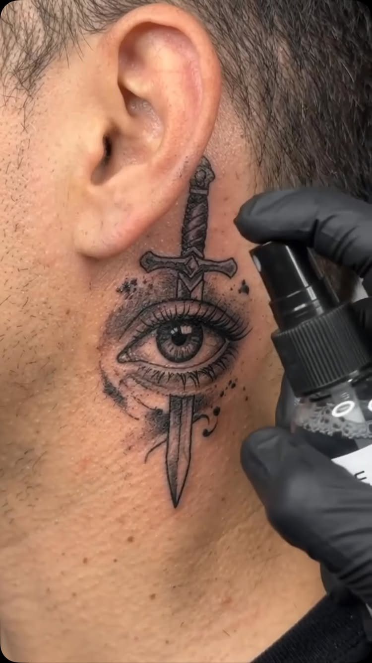 Sword piercing through an eye tattoo on a man's neck being sprayed.
