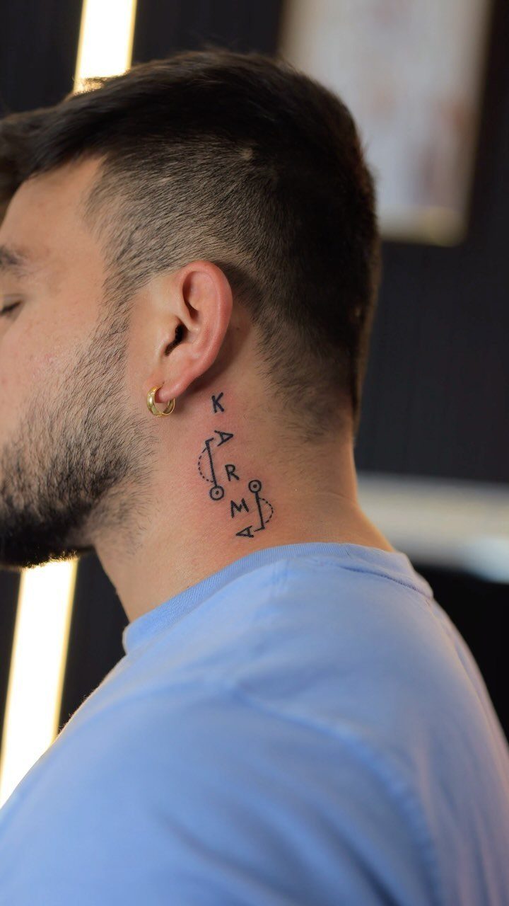 Man's neck with a vertical black ink tattoo spelling the word KARMA