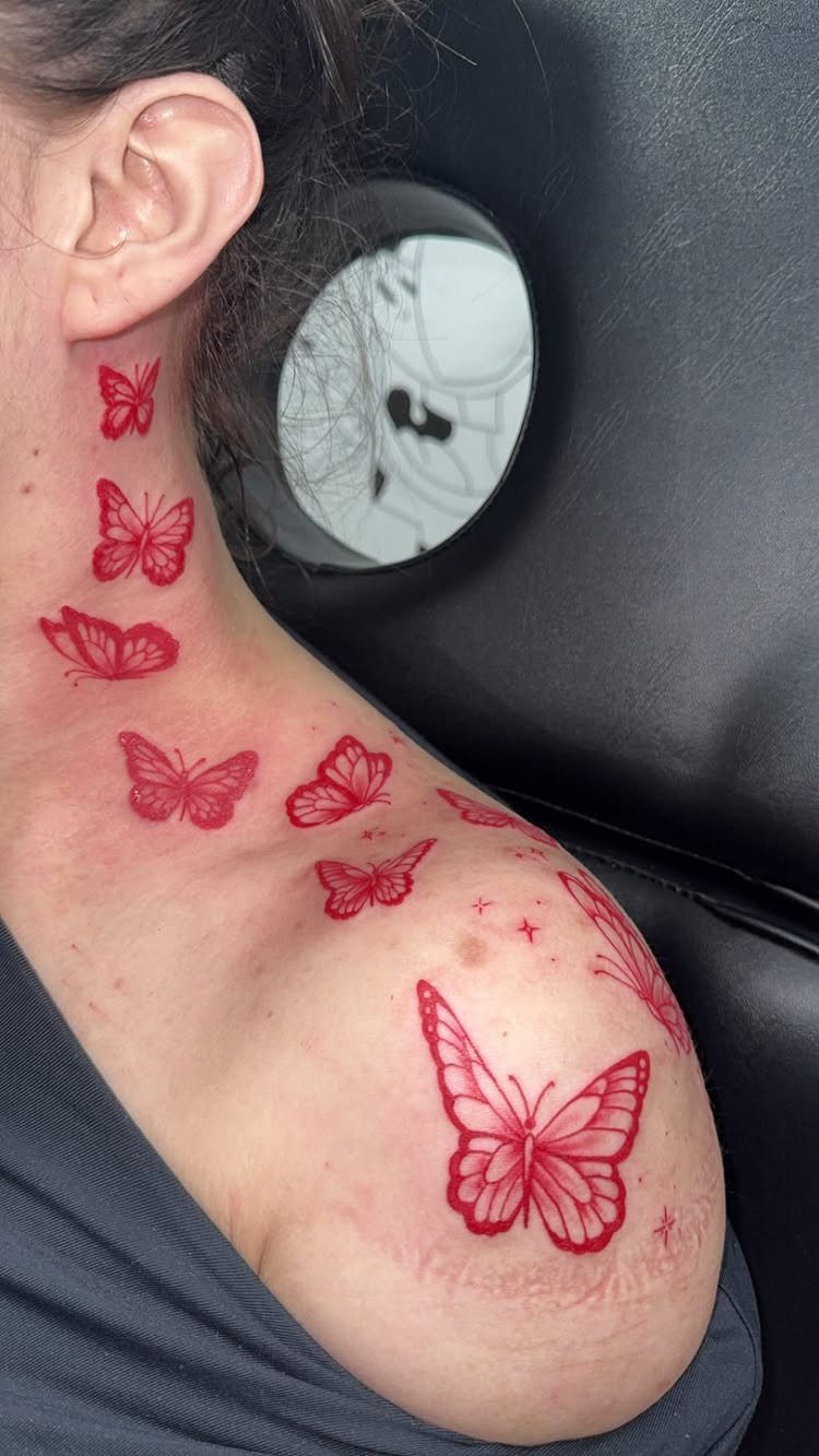Red butterfly tattoos on a woman's neck and shoulder against a dark background