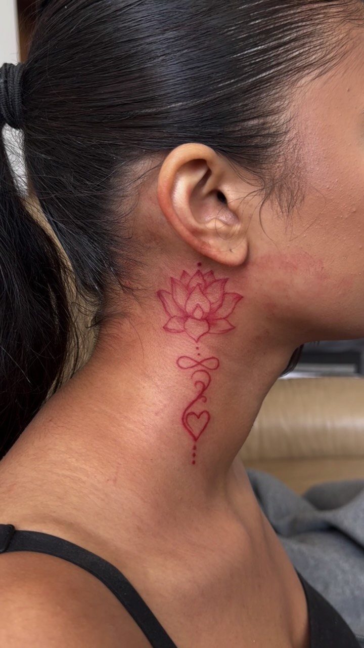 Woman's neck with a red lotus, infinity symbol, and heart tattoo.