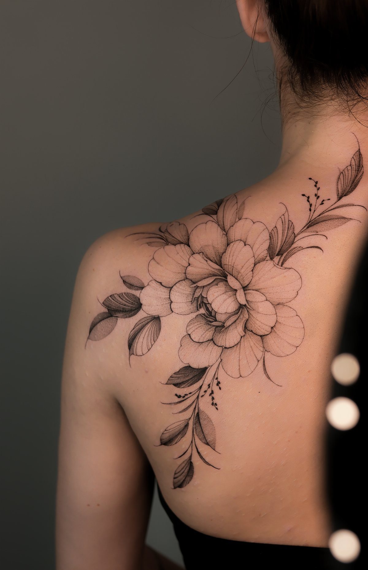 Floral peony tattoo in black ink on a woman's upper back and shoulder