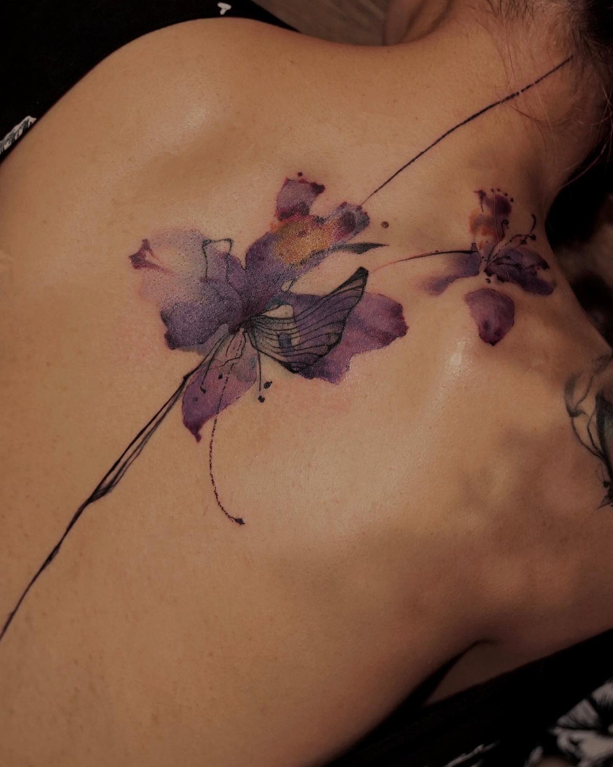 Watercolor purple butterfly tattoo on a woman's upper back and shoulder