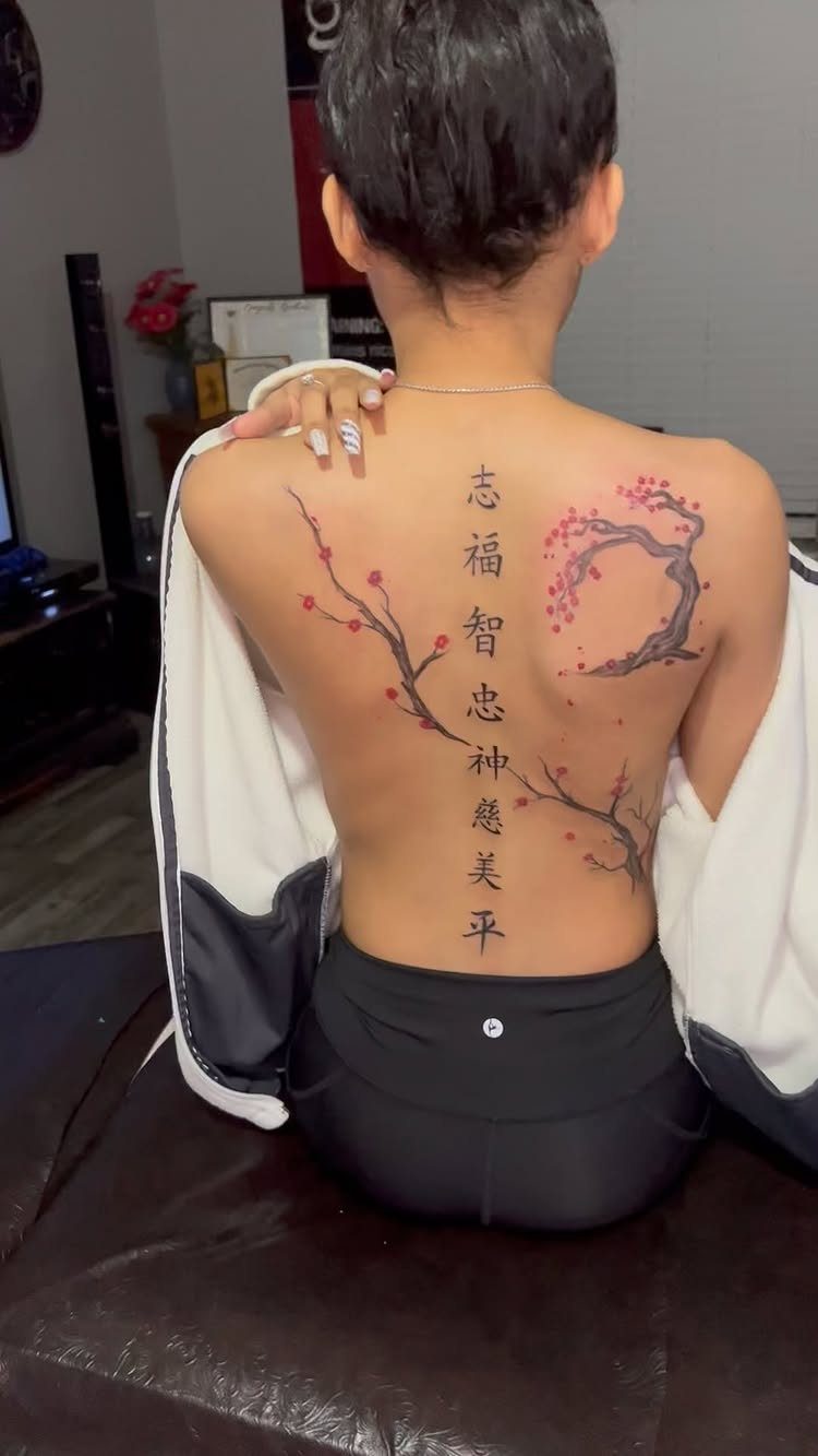 Woman's back with a cherry blossom branch and Japanese character tattoo.