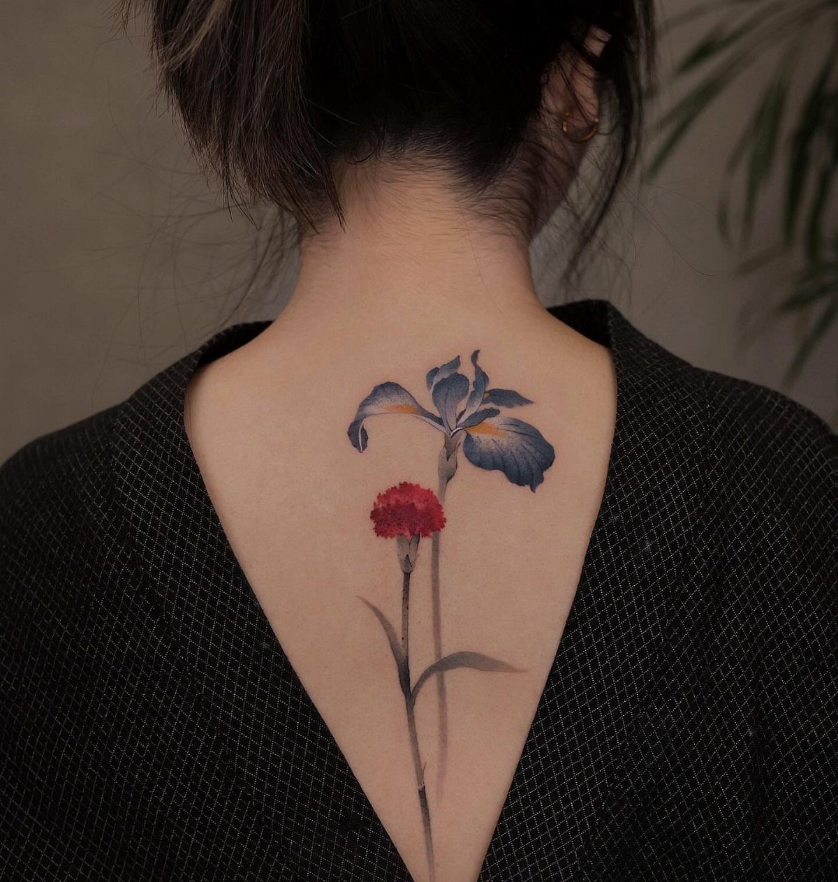 Woman's upper back featuring a colorful floral tattoo of a blue iris and red carnation.