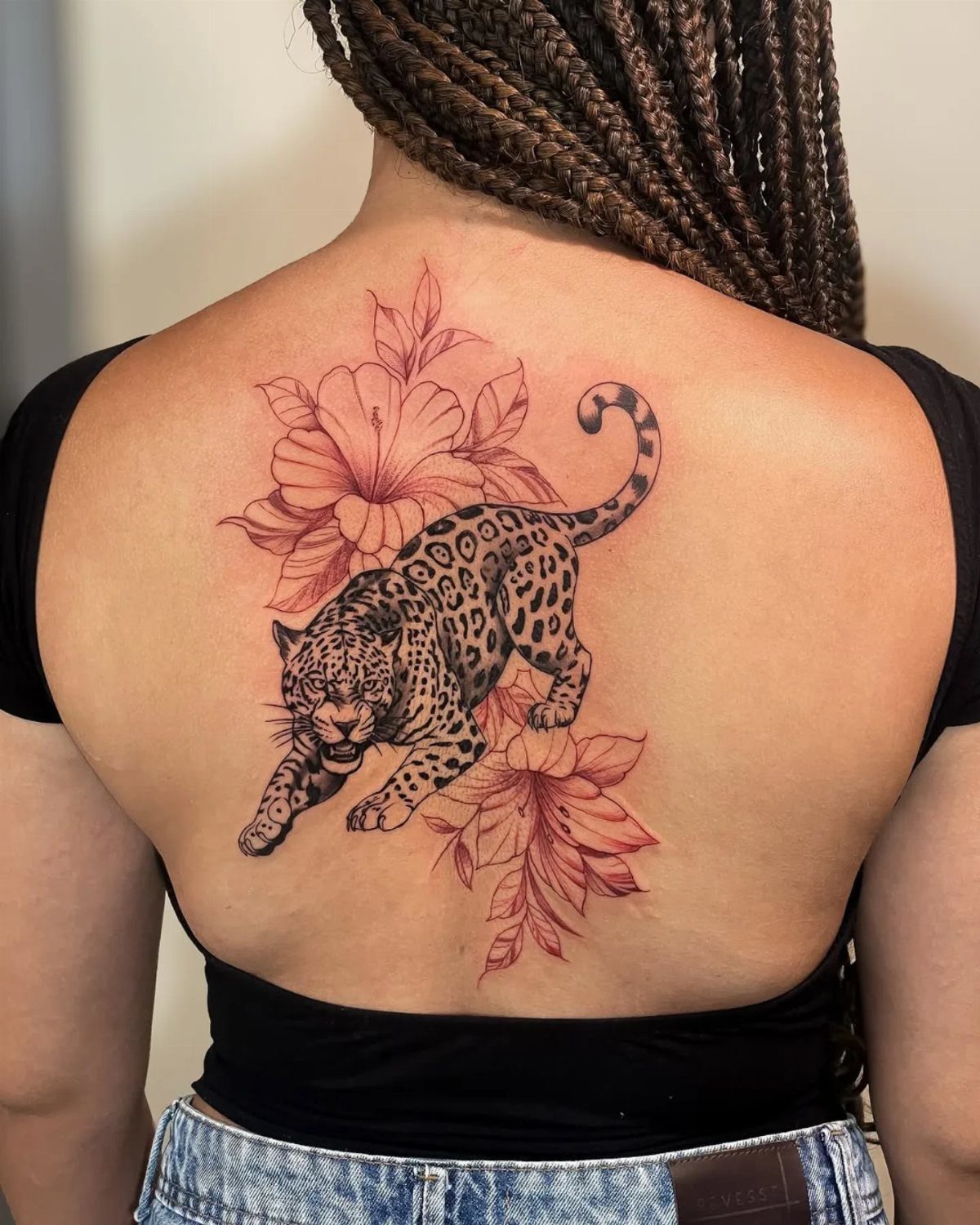 Spotted leopard tattoo with red flowers on a woman's upper back