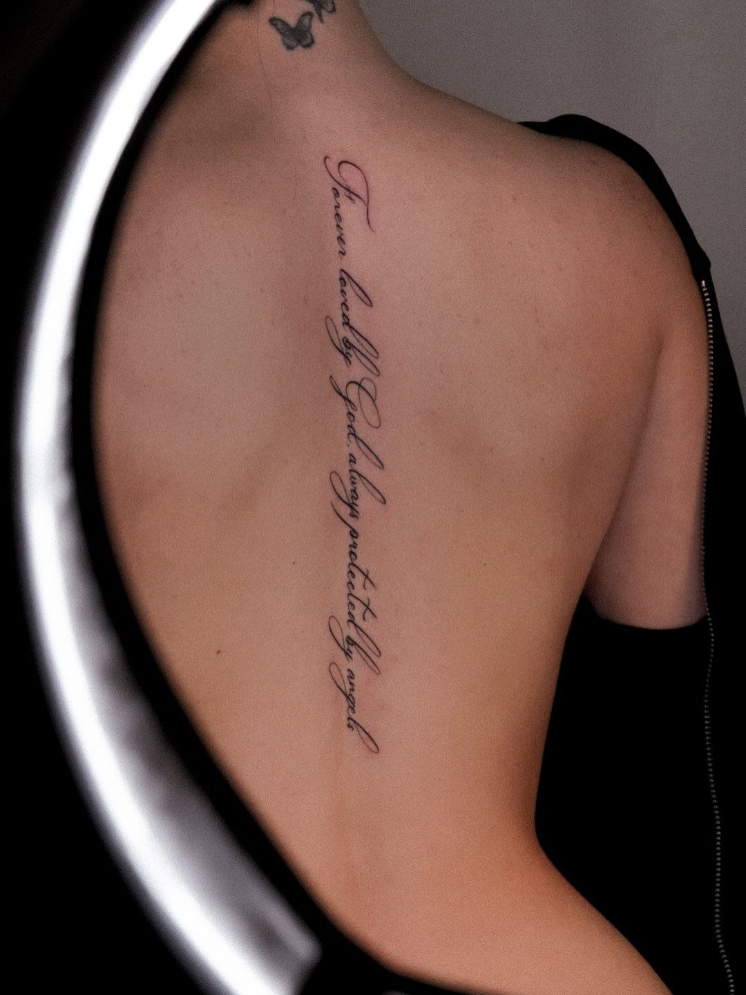 Cursive text tattoo running vertically down the center of a woman's spine