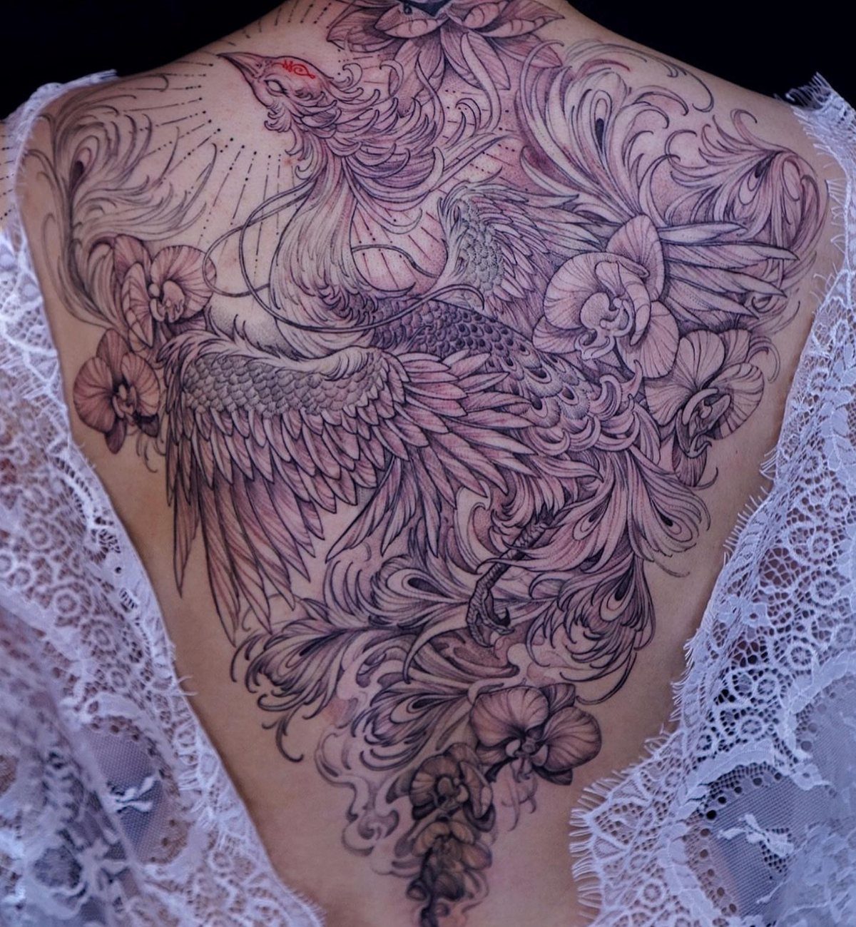 Phoenix tattoo with orchids covering a woman's back, featuring intricate purple and black ink.