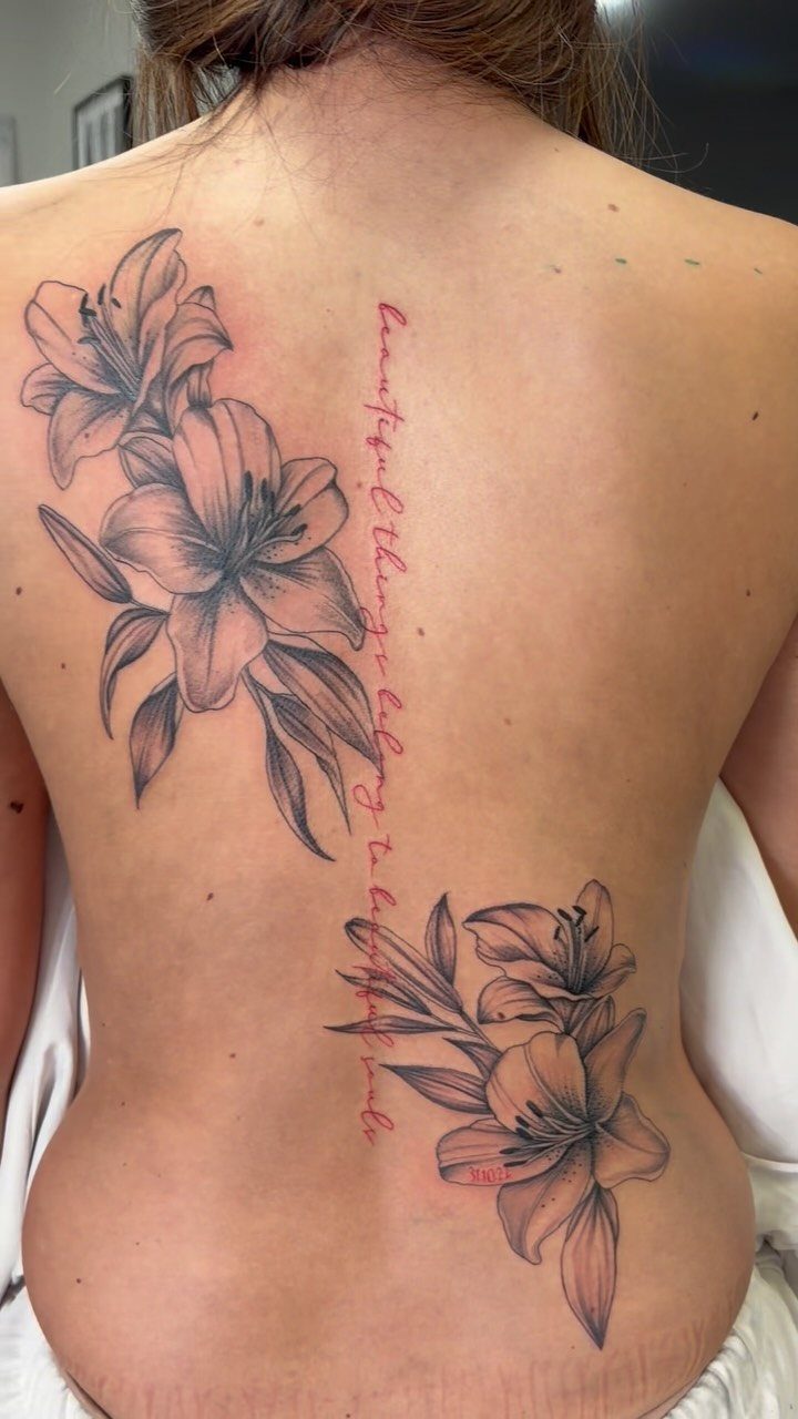 Woman's back with lily flower tattoos and a red script quote on the spine