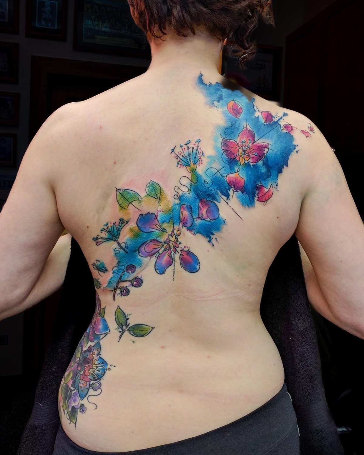 Watercolor floral tattoo with blue and pink flowers on a person's back.