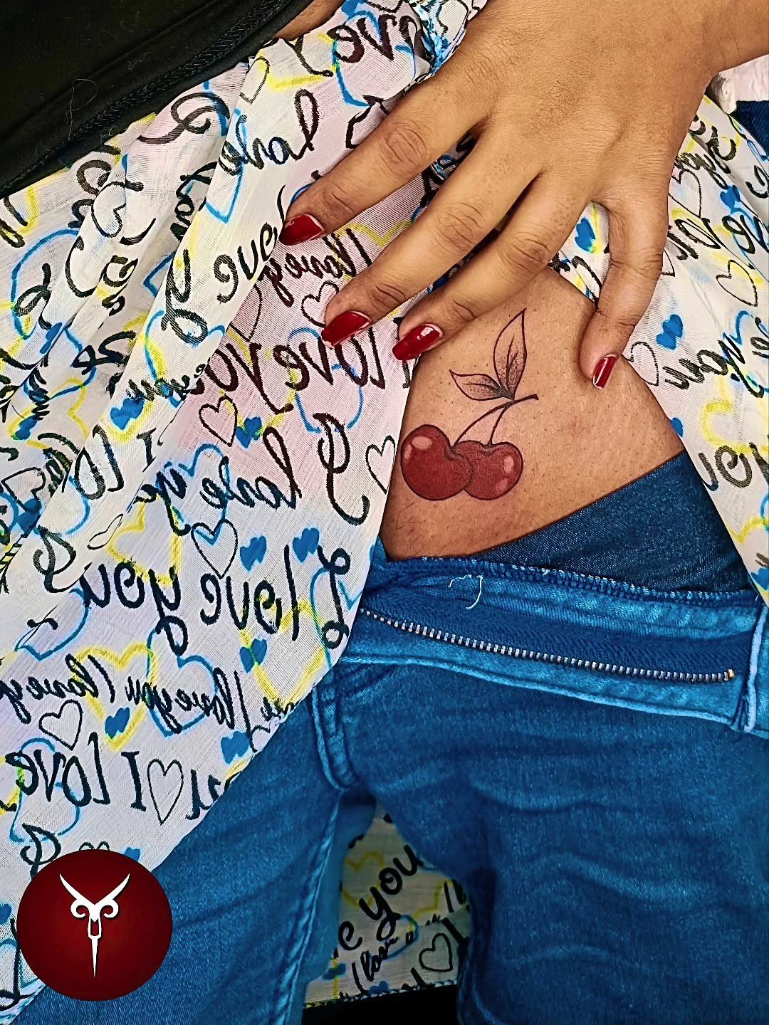Red cherry tattoo with green stem on a person's hip and thigh.