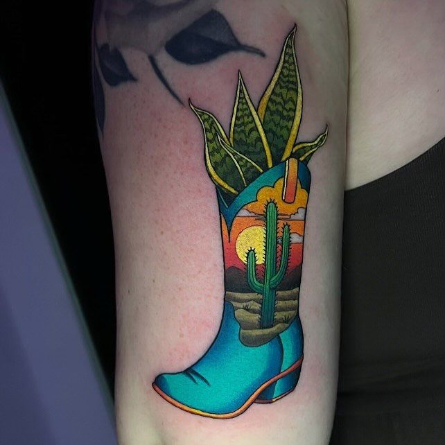 Colorful cowboy boot tattoo with a desert sunset and succulent plant on skin