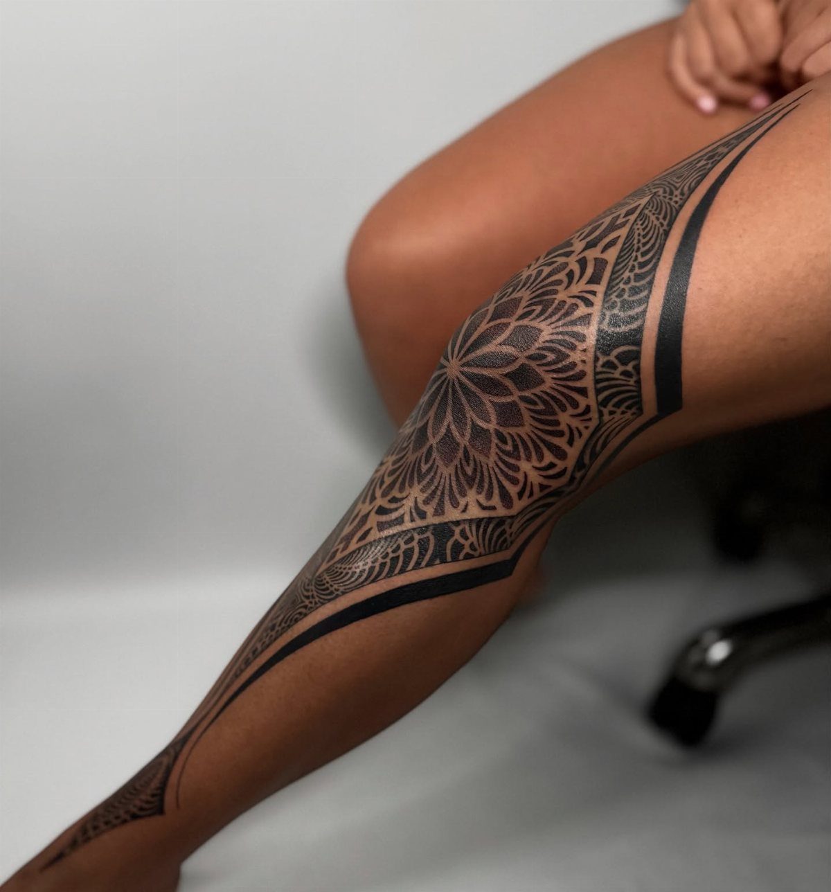 Intricate black ink mandala tattoo on a person's knee and leg.