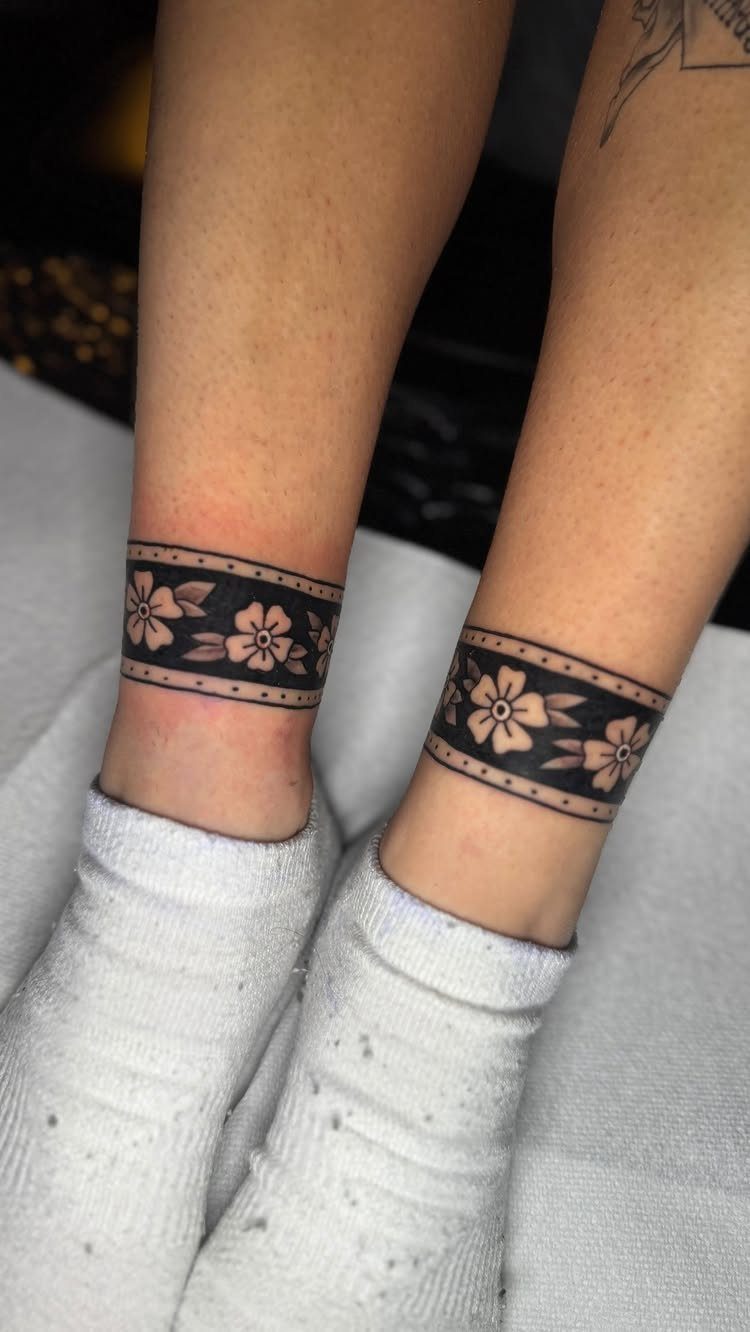 Matching floral band tattoos on two ankles wearing white socks