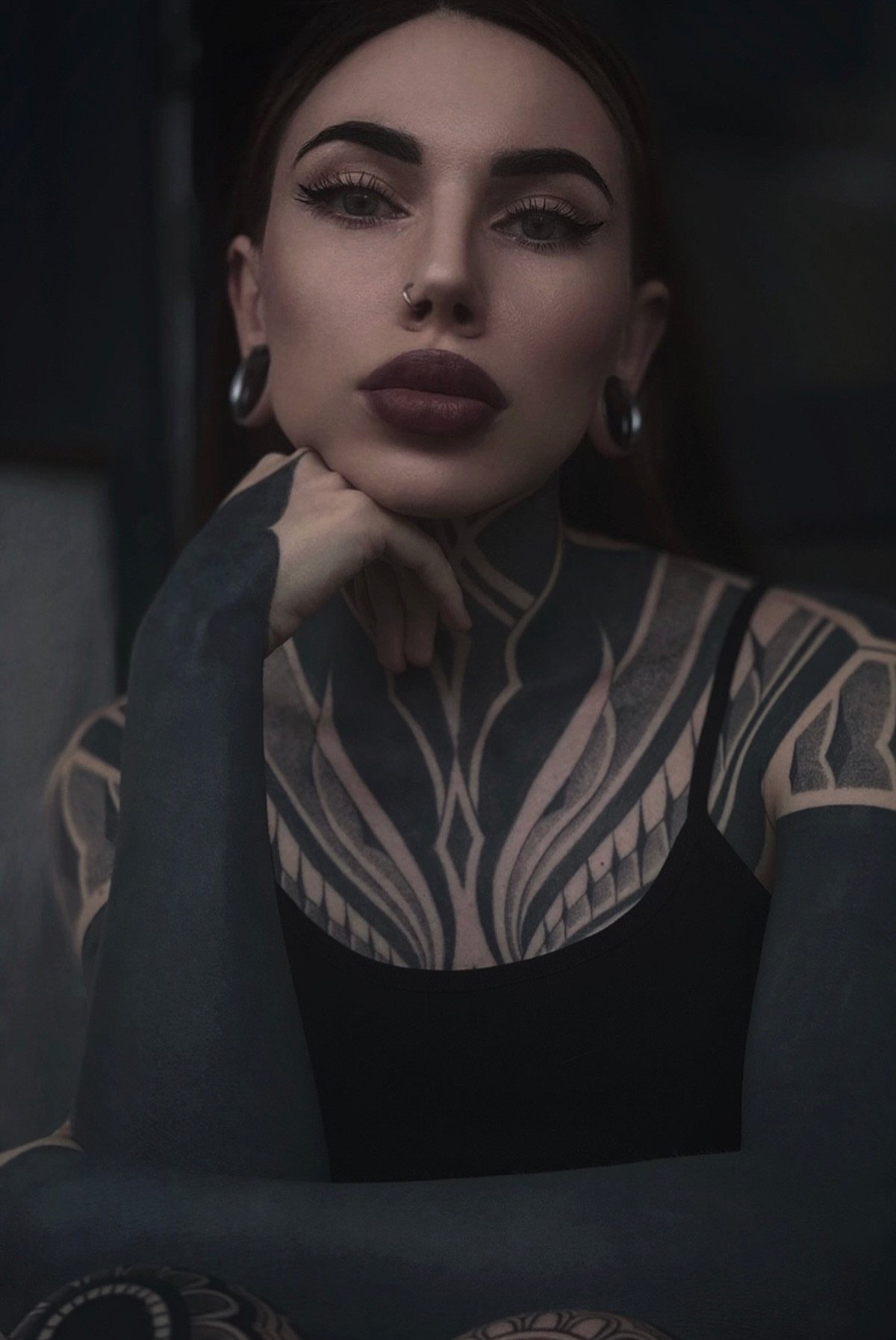 Woman with ornamental black ink tattoos on her chest, neck, and arms.