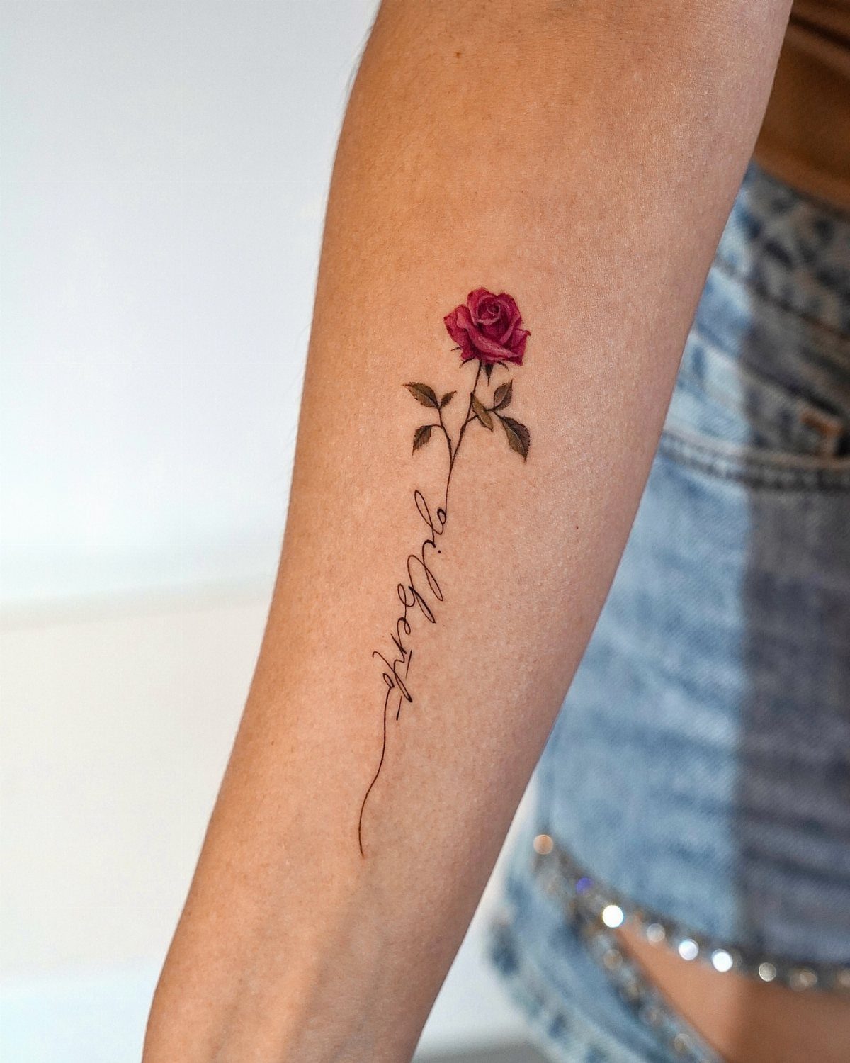 Red rose tattoo with cursive name Gilbert on a person's forearm