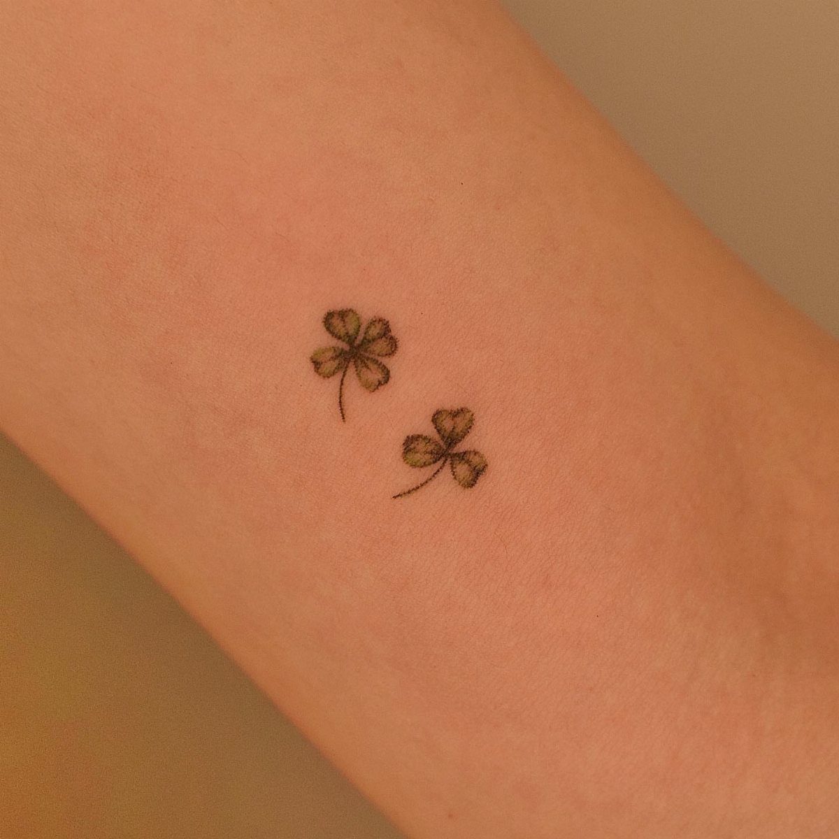 Two small green clover tattoos, one four-leaf and one three-leaf, on an arm.