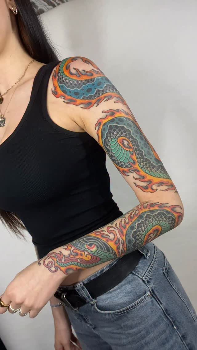 Colorful snake tattoo wrapping around a woman's arm from shoulder to wrist.