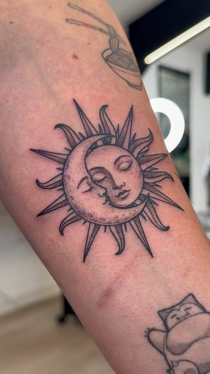 Sun and moon combined tattoo with radiating beams on a person's arm.