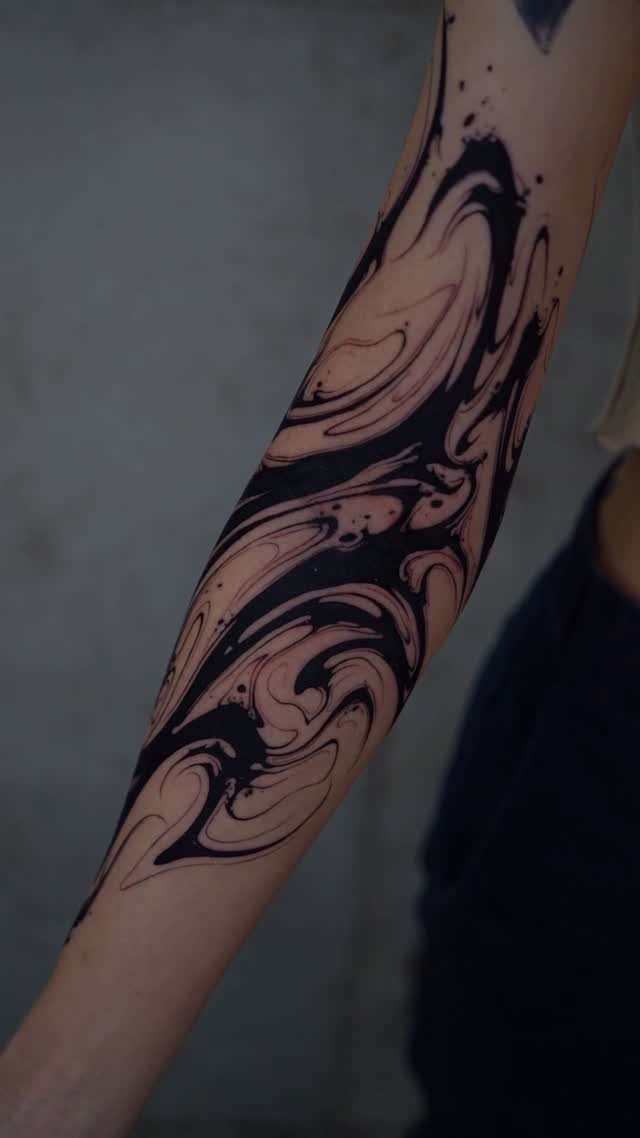 Forearm tattoo with black swirling organic shapes and fluid cohesive design flow.