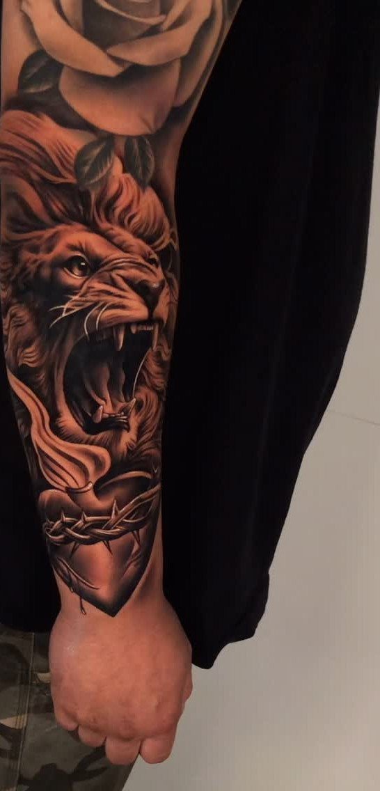 Roaring lion tattoo on a man's forearm with a rose and crowned heart.