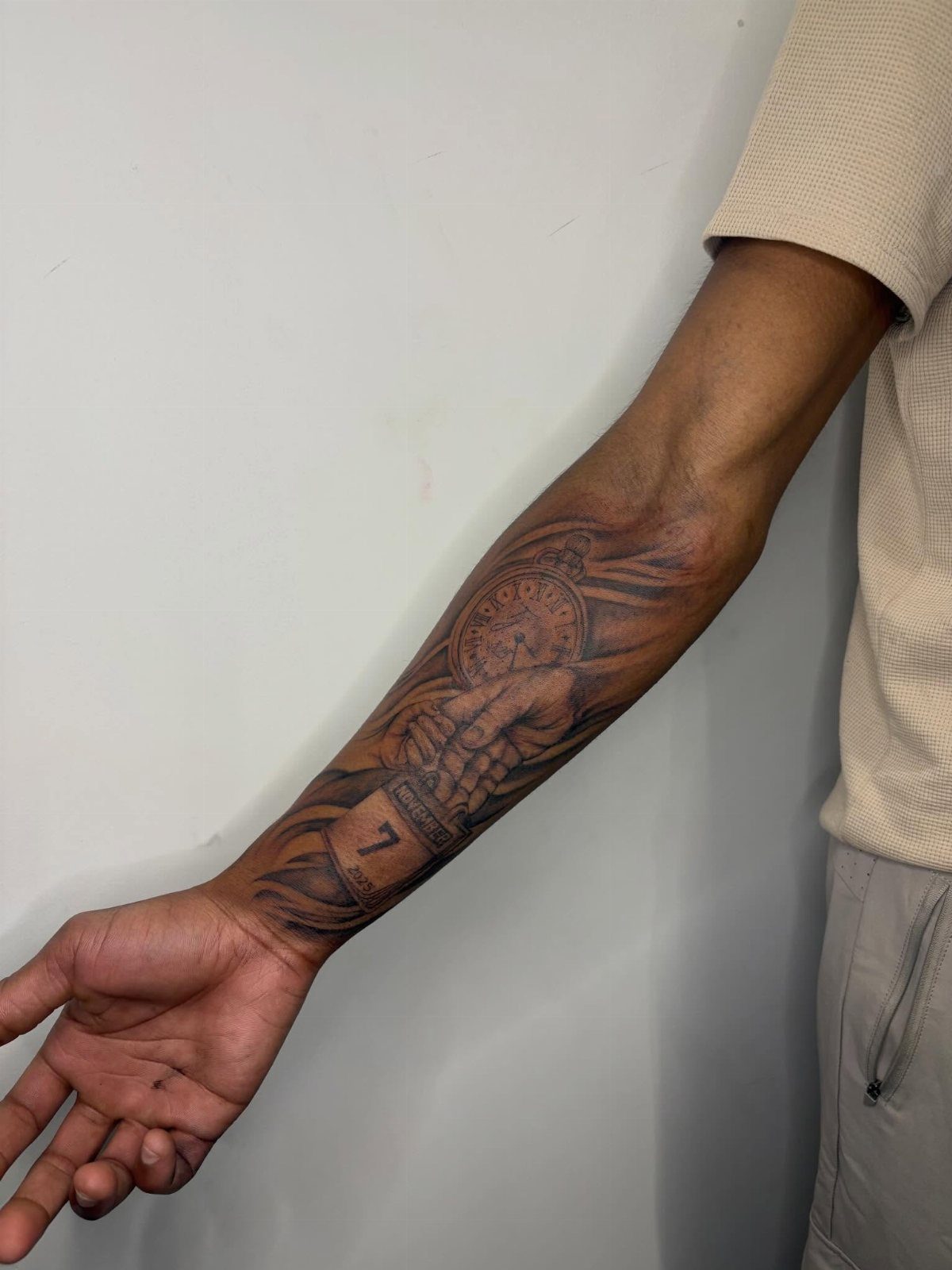 Forearm tattoo of a hand holding a pocket watch with a numbered banner.