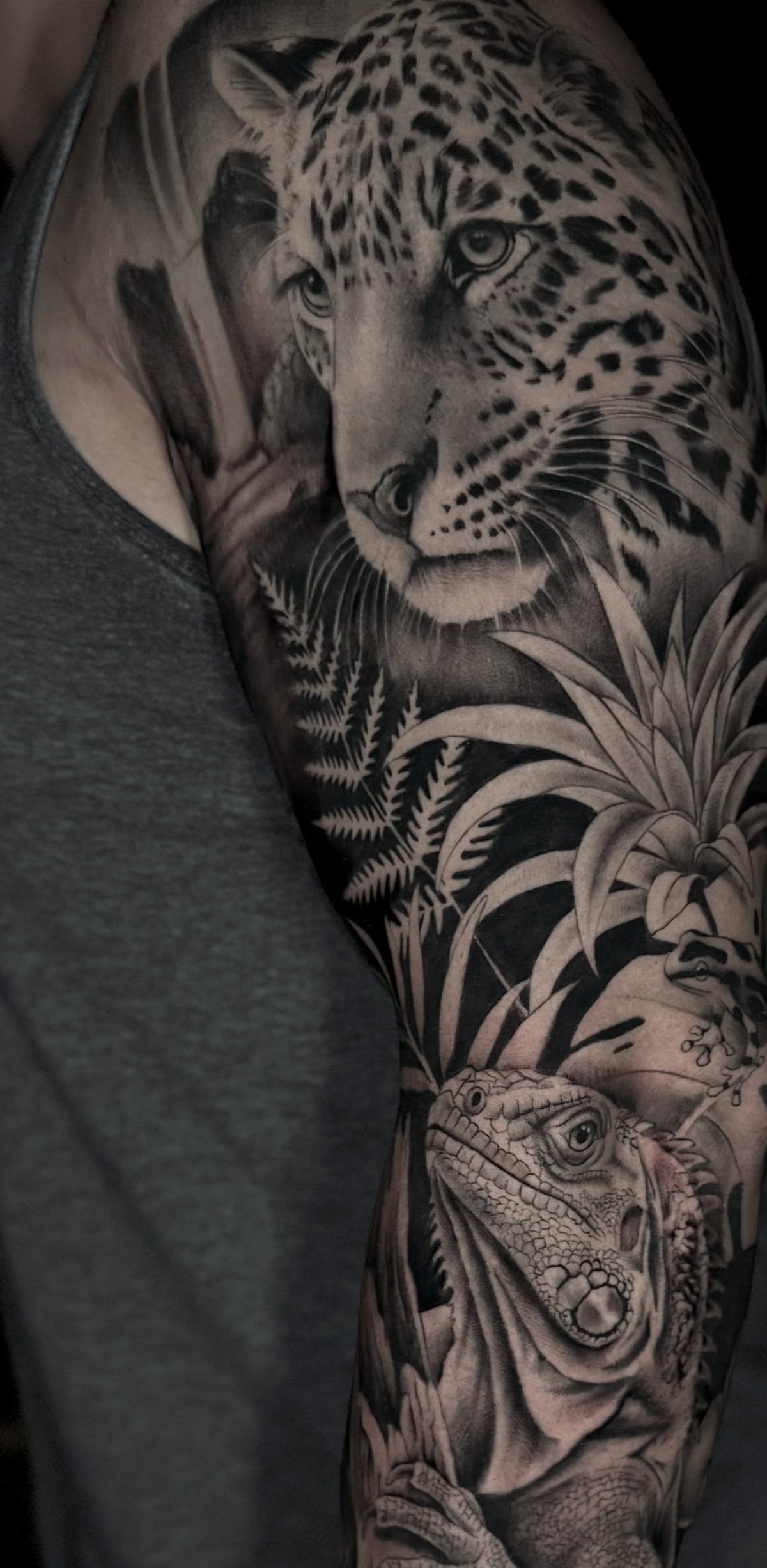 Leopard, iguana, and tropical leaves in a black and grey arm tattoo.