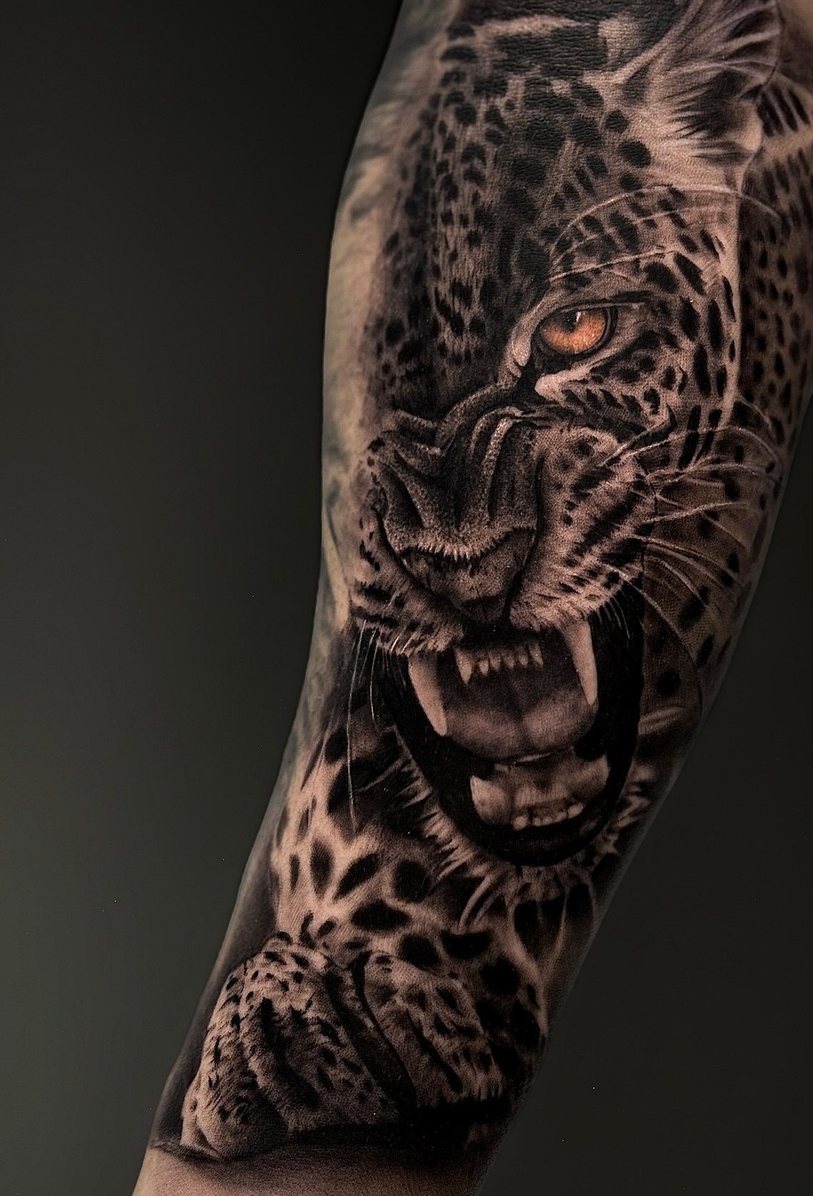 Leopard realism tattoo on an arm with a striking orange eye.