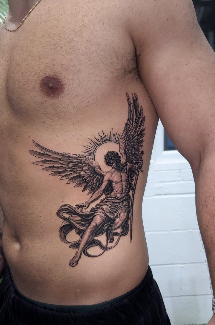 Detailed black ink angel tattoo on the ribcage of a muscular man.
