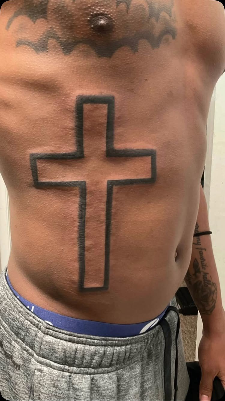 Large black outlined cross tattoo on the rib cage of a man's torso
