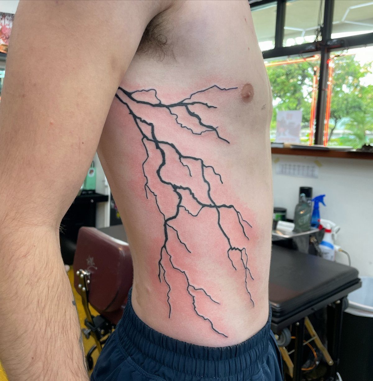 Lightning bolt tattoo on a man's ribs with red skin from the process.