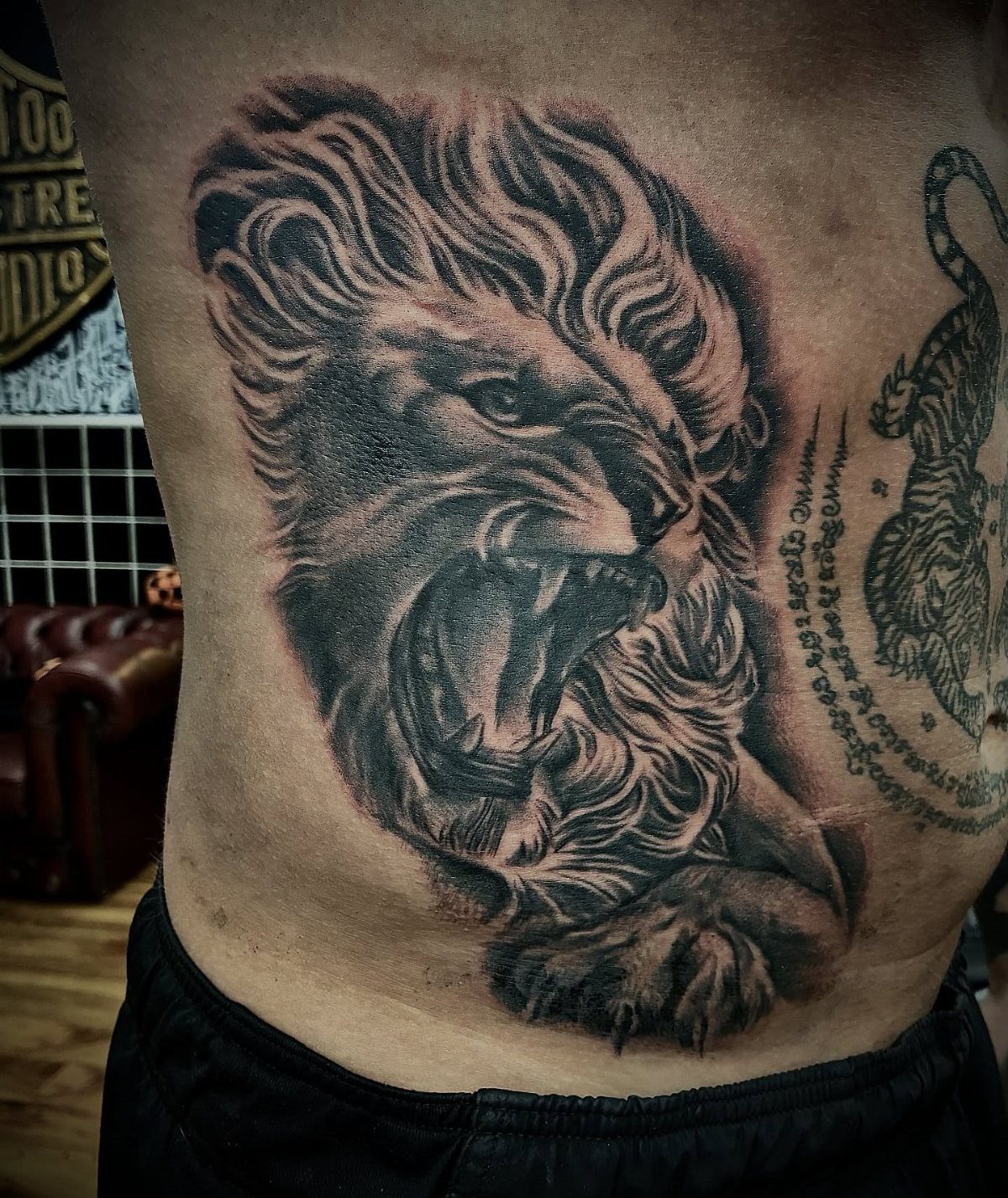 Roaring lion head tattoo in black and grey ink on a man's ribcage.