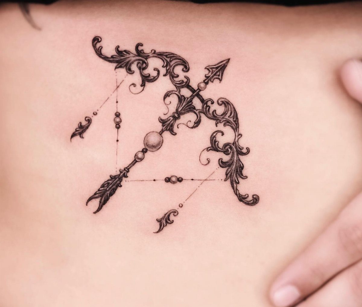 Ornate black ink arrow tattoo with filigree and geometric lines on a person's ribs
