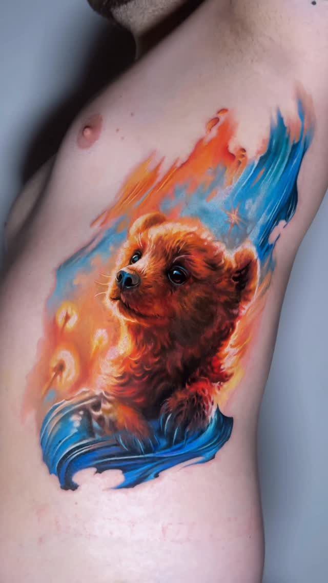 Realistic bear cub tattoo on a man's ribs with fire and water effects.
