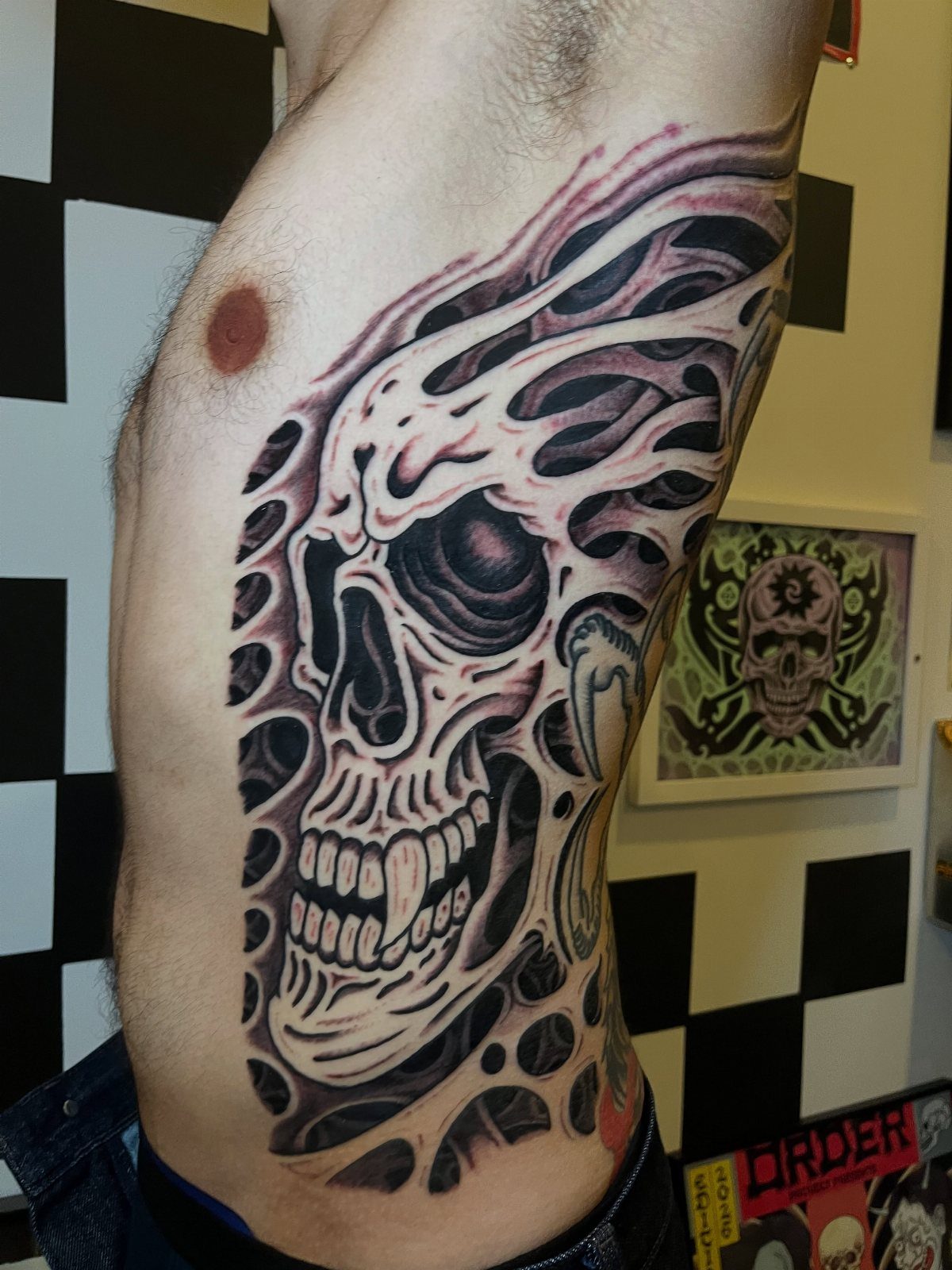 Stylized skull tattoo with organic flowing patterns on a man's ribcage.