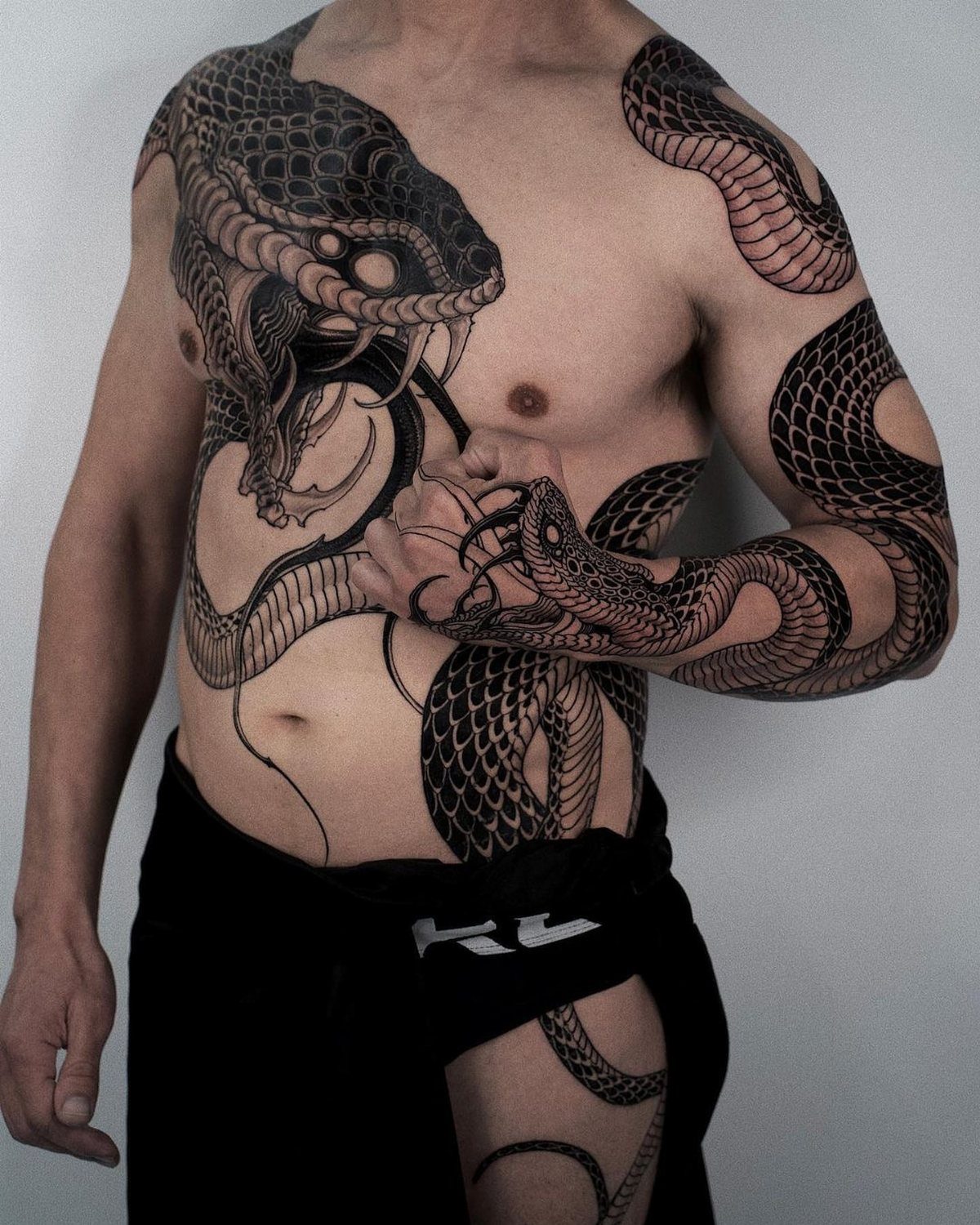 Man with large black snake tattoos covering his chest, ribs, and left arm.