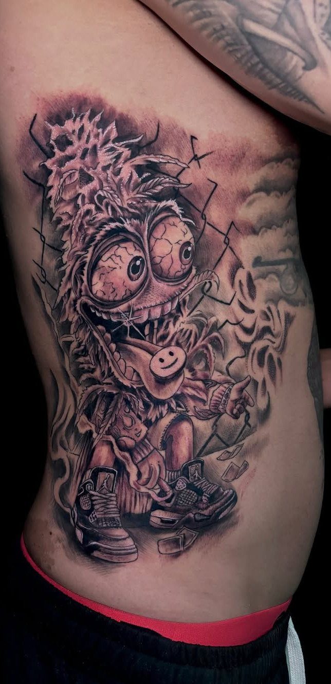 Detailed black and grey monster tattoo on a man's ribcage with smoky background.