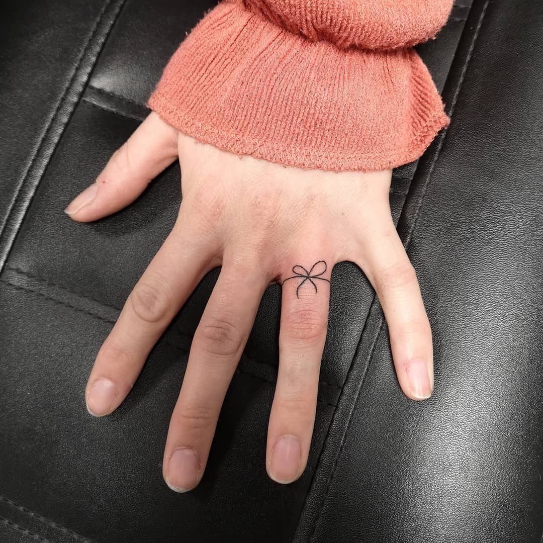 Small black bow tie tattoo on the ring finger of a hand