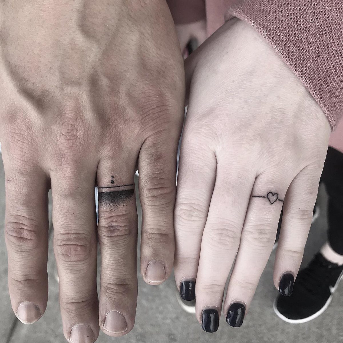 Two ring fingers with minimalist black band tattoos, one featuring a small heart.