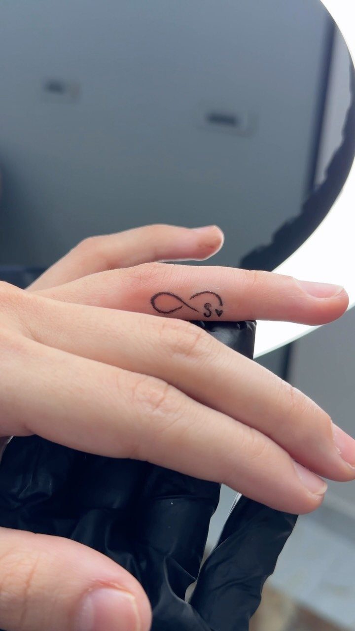 Infinity symbol and heart tattoo on the ring finger of a person's hand.