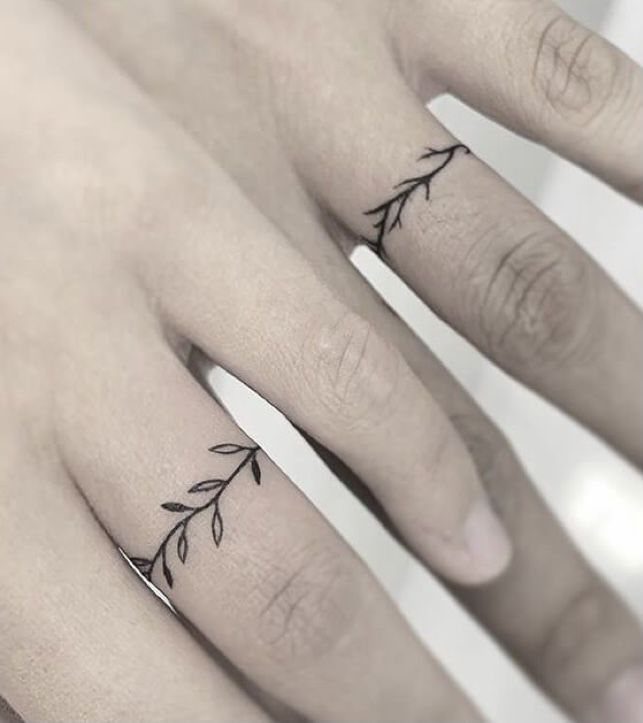 Leafy vine tattoos wrapped around the ring fingers of two people's hands.