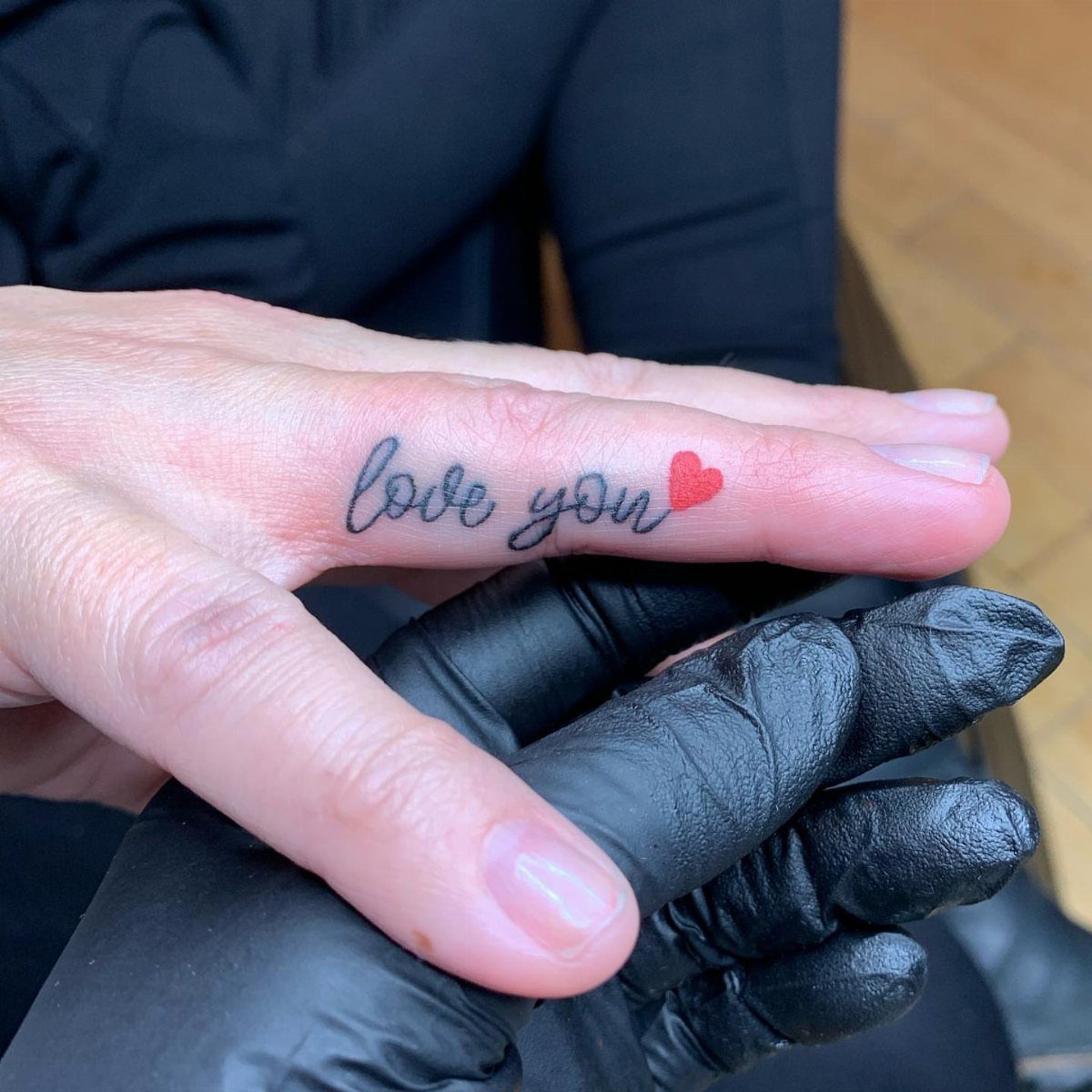 Ring finger tattoo with the phrase love you and a small red heart.