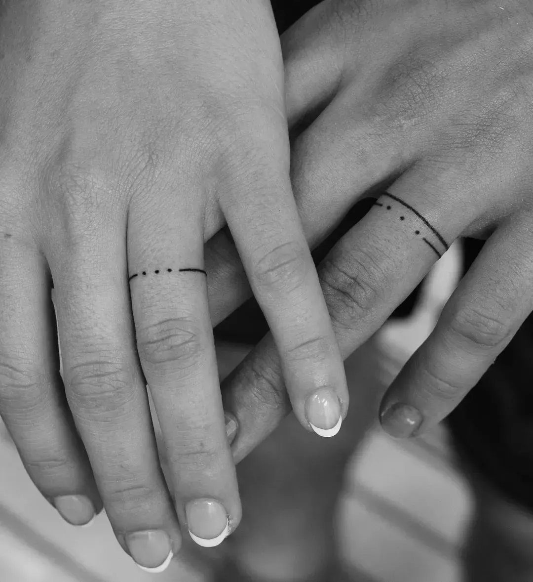 Two ring fingers featuring thin band tattoos with three small centered dots.