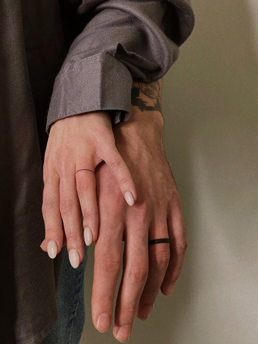 Two hands with matching thin black band tattoos on their ring fingers.