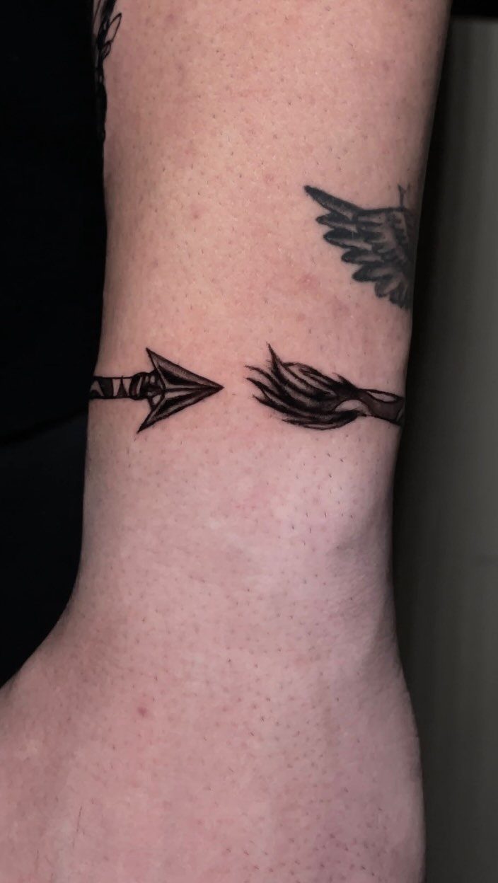 Arrow ring tattoo wrapping around a person's wrist in black ink.