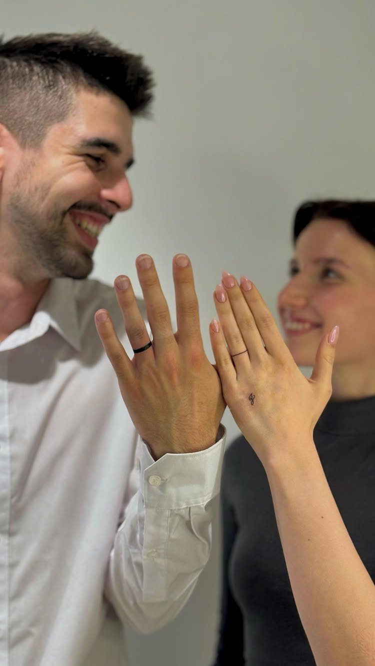 Man and woman showing thin black ink ring tattoos on their fingers.