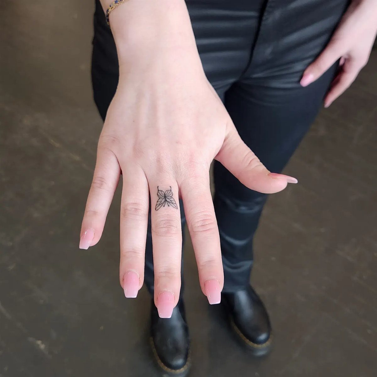 Small black butterfly tattoo on a finger with light pink manicured nails.