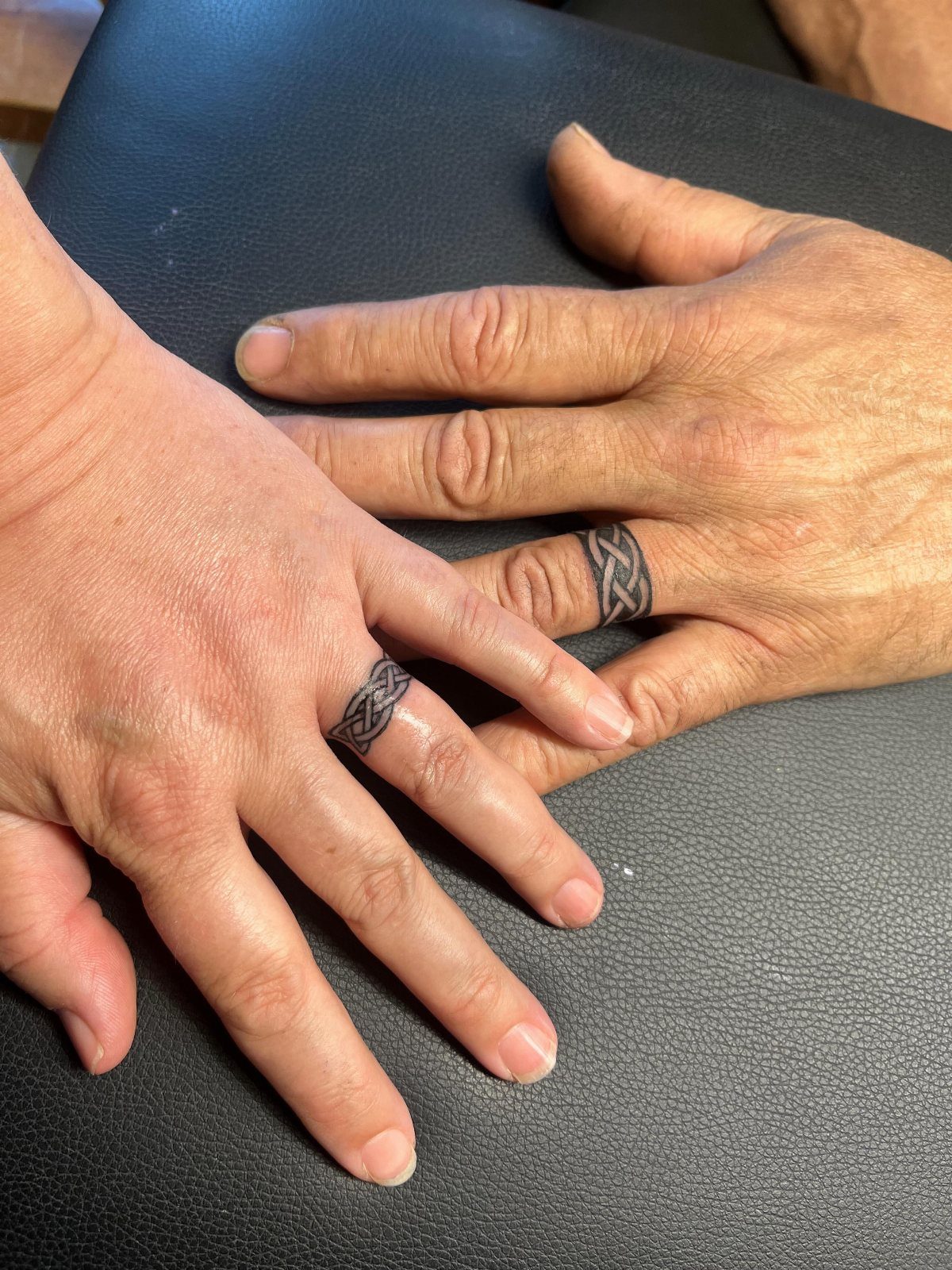 Two hands with matching black Celtic knot ring tattoos on their ring fingers.
