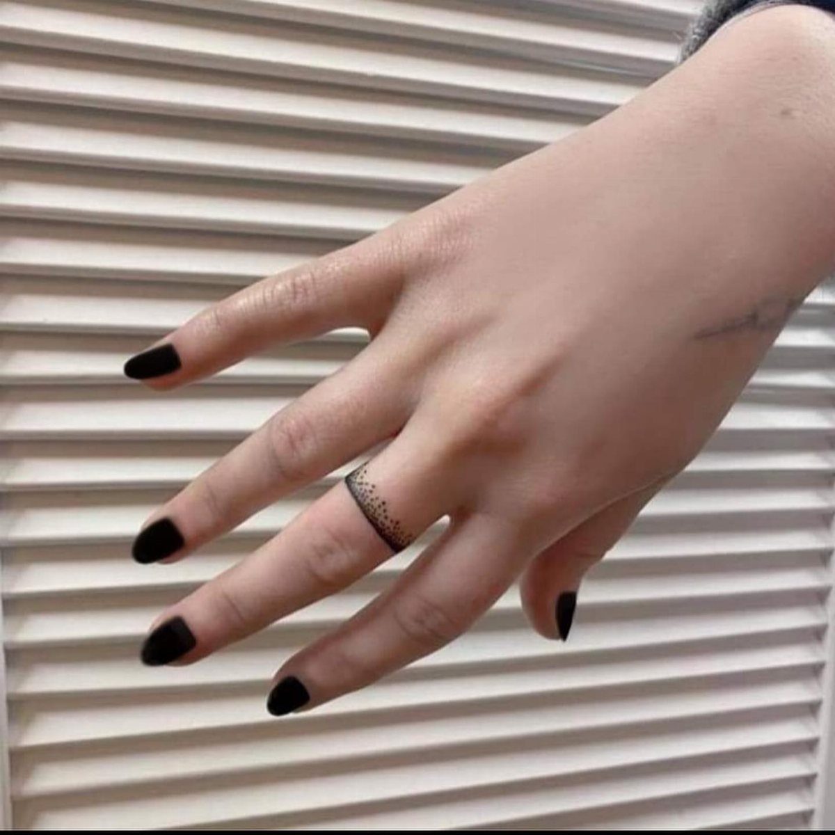 Hand with black nails and a dotted ring tattoo on the ring finger.