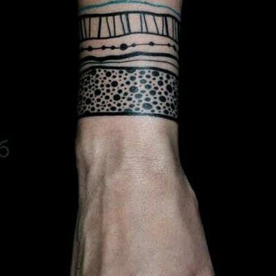 Wrist with multiple black ink geometric band tattoos including lines and dots.
