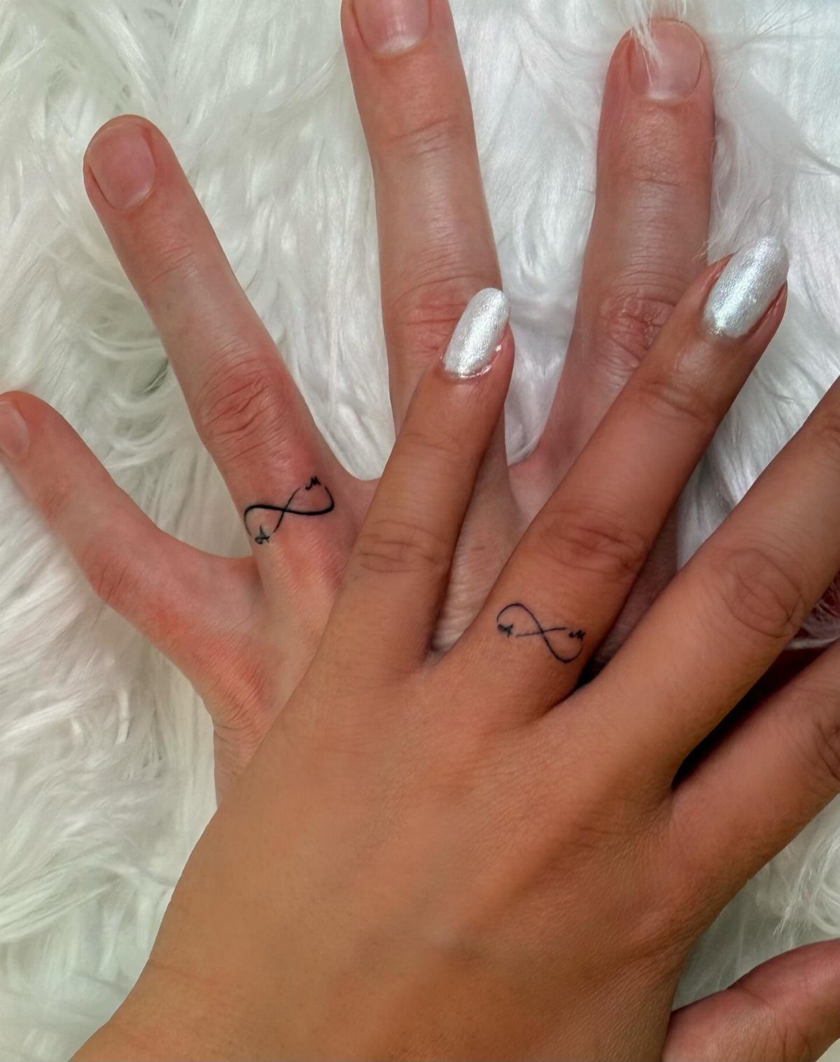 Two ring fingers featuring matching black ink infinity symbol tattoos on white fur.